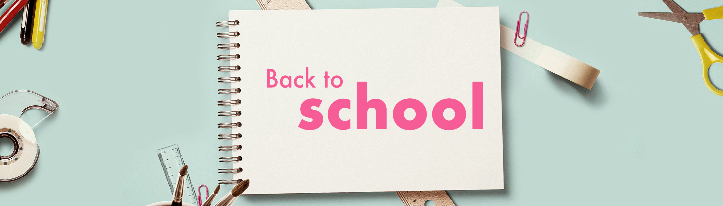 Et skrivebord med saks, lineal, tape og lignende remedier liggende. En stor blok papir hvorpå der står ’Back to school’.